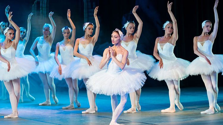  Zehn Ballerinas in Tutus tanzen gemeinsam auf einer Bühne.